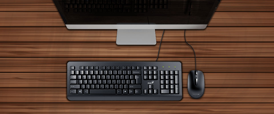 Vista superior de un escritorio de madera con un Teclado y Mouse Genius KM-160 USB y la parte inferior de un monitor de computadora.