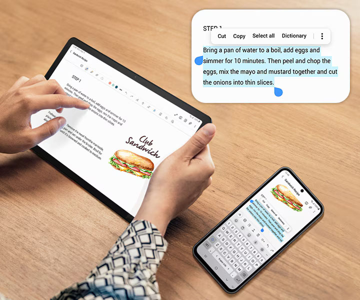 Una persona está tocando Galaxy Tab A9+. A la derecha hay un teléfono inteligente Galaxy. Ambos dispositivos muestran la misma pantalla. El teléfono inteligente tiene una parte del texto seleccionada en azul, para indicar la función de copiar y pegar en todos los dispositivos. Arriba de los dispositivos está la parte seleccionada ampliada, con opciones para seleccionar todo, cortar, copiar, compartir y más.