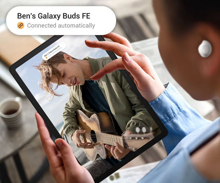 Una persona está usando Galaxy Tab A9+ con Galaxy Buds FE encendidos. En la pantalla se puede ver a un hombre tocando la guitarra. Hay una notificación en la parte superior de la pantalla y la versión ampliada de la misma notificación se puede ver en la esquina superior izquierda. La notificación dice Ben's Galaxy Buds FE y la siguiente línea tiene un ícono de enlace con el texto Conectado automáticamente.